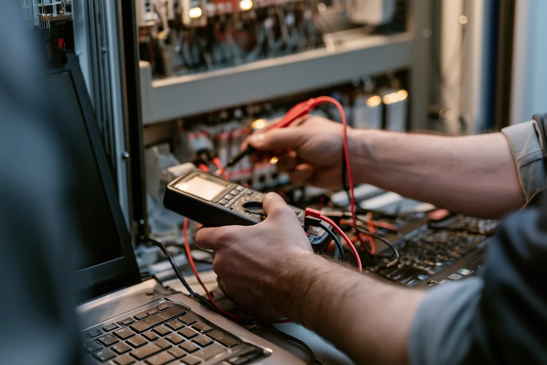 Engineer diagnosing a control system with a multimeter and laptop